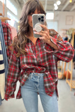 Load image into Gallery viewer, Person wearing a red plaid shirt and light blue jeans in a clothing store.
