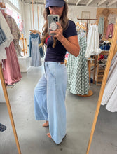 Load image into Gallery viewer, Woman taking a mirror selfie wearing a dark top and light blue jeans in a clothing store.