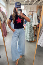 Load image into Gallery viewer, Person taking a mirror selfie wearing a black t-shirt with a red star, light blue jeans, and a blue cap in a clothing store.