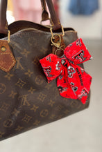 Load image into Gallery viewer, Brown patterned handbag with a red bow keychain on a light surface.