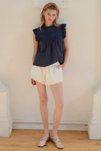 Load image into Gallery viewer, Woman wearing a navy top and white shorts standing against a plain wall.