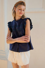 Load image into Gallery viewer, Young girl wearing a navy blue top with ruffled sleeves and white shorts against a neutral wall.
