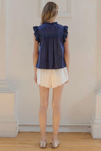 Load image into Gallery viewer, Woman wearing a navy blue top with ruffled sleeves and white shorts in a room.