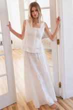 Load image into Gallery viewer, Woman wearing a white outfit standing in a bright room with large windows.