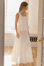 Load image into Gallery viewer, Woman wearing a white dress standing in a room with wooden floor and white walls.