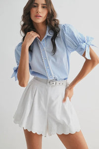 Woman wearing a blue striped shirt and white shorts on a plain background