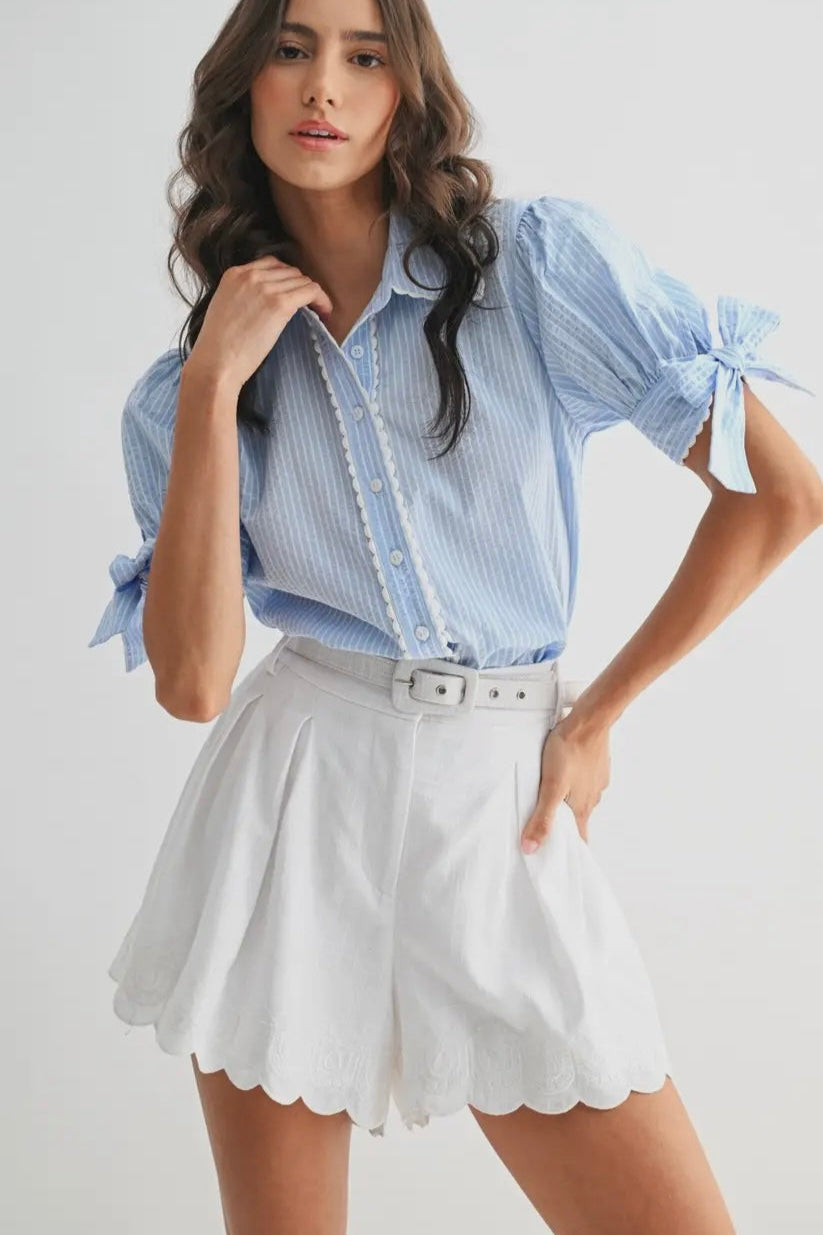 Woman wearing a blue striped shirt and white shorts on a plain background