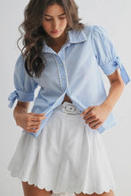 Load image into Gallery viewer, Woman wearing a light blue striped shirt with tied sleeves and a white skirt on a plain background