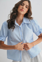 Load image into Gallery viewer, Woman wearing a light blue striped shirt with ruffled details on a plain background
