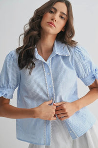 Woman wearing a light blue striped shirt with ruffled details on a plain background