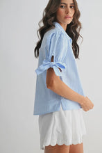 Load image into Gallery viewer, Woman wearing a light blue striped shirt with rolled-up sleeves on a white background