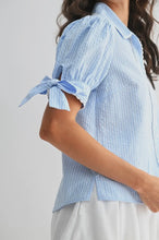 Load image into Gallery viewer, Woman wearing a light blue checkered blouse with tied sleeves on a plain background