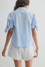 Load image into Gallery viewer, Woman wearing a light blue striped shirt with tied sleeves and white shorts on a plain background