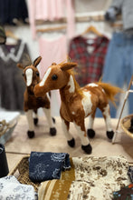 Load image into Gallery viewer, Two plush toy horses on a table with clothing items in the background
