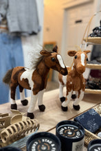 Load image into Gallery viewer, Two plush horse toys on a store shelf with clothing and accessories in the background.