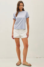 Load image into Gallery viewer, Woman wearing a light blue and white color-blocked t-shirt and white shorts on a plain background