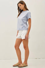 Load image into Gallery viewer, Woman wearing a light blue t-shirt and white shorts on a plain background