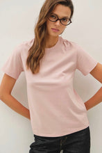 Load image into Gallery viewer, Woman wearing a light pink t-shirt and dark jeans against a plain background