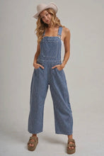 Load image into Gallery viewer, A woman modeling blue and white vertically striped corduroy overall jumpsuit with a beige wide-brim hat and brown platform sandals, standing against a light gray studio background.