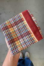 Load image into Gallery viewer, Plaid fabric with a red border held by a hand on a concrete floor.