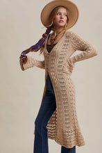 Load image into Gallery viewer, Woman wearing a long beige cardigan, blue jeans, and a wide-brimmed hat on a plain background