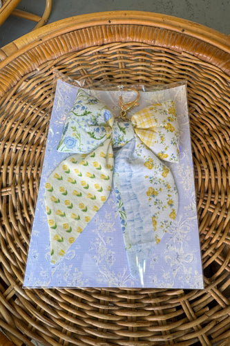Packaged fabric bow with floral pattern on a wicker surface