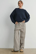 Load image into Gallery viewer, Woman wearing a navy sweater and checkered pants against a plain background