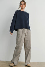 Load image into Gallery viewer, Woman wearing a navy sweater and checkered pants against a white background