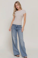 Load image into Gallery viewer, Woman wearing a beige top and blue flared jeans on a plain background