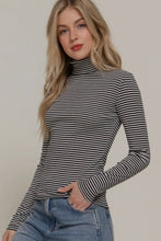 Load image into Gallery viewer, Woman wearing a black and white striped turtleneck sweater with blue jeans on a plain background