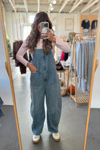 Load image into Gallery viewer, Person wearing denim overalls taking a mirror selfie in a clothing store.