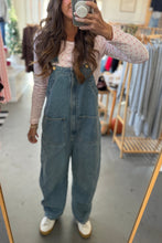Load image into Gallery viewer, Person wearing denim overalls taking a mirror selfie in a store.