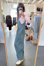 Load image into Gallery viewer, Person wearing denim overalls taking a mirror selfie in a clothing store.