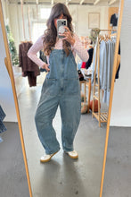 Load image into Gallery viewer, Person wearing denim overalls taking a mirror selfie in a clothing store.