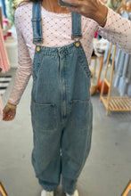 Load image into Gallery viewer, Person wearing denim overalls and a patterned top in a clothing store.