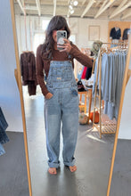 Load image into Gallery viewer, Person wearing denim overalls taking a mirror selfie in a clothing store.