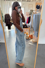 Load image into Gallery viewer, Person wearing a brown top and light blue jeans standing in front of a mirror in a clothing store.