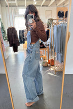 Load image into Gallery viewer, Person wearing denim overalls taking a mirror selfie in a clothing store.