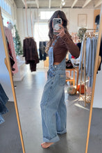Load image into Gallery viewer, Person wearing denim overalls taking a mirror selfie in a clothing store.