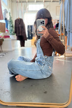 Load image into Gallery viewer, Person wearing a denim overalls sitting on the floor in a clothing store.