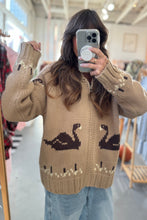 Load image into Gallery viewer, Person wearing a brown sweater with swan designs in a store setting