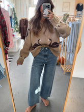 Load image into Gallery viewer, Person wearing a beige sweater with deer designs and blue jeans, standing in a store.