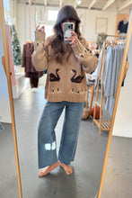 Load image into Gallery viewer, Person wearing a beige sweater with black swan designs in a clothing store.