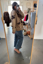 Load image into Gallery viewer, Person taking a mirror selfie wearing a beige sweater with animal prints and blue jeans in a clothing store.