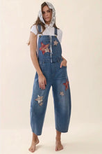 Load image into Gallery viewer, Woman wearing blue denim overalls with star patches on a beige background