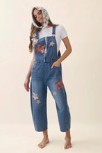 Load image into Gallery viewer, Woman wearing blue denim overalls with star patches on a beige background